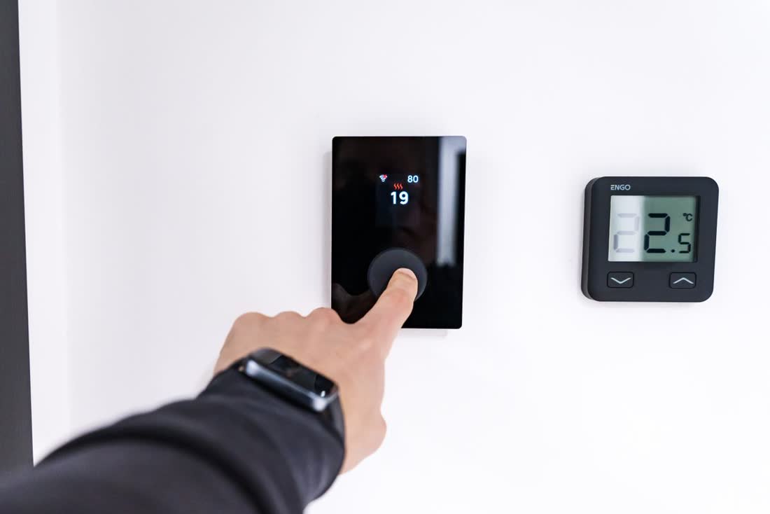 Mano ajustando un termostato digital de pared